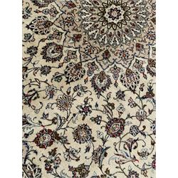 Persian Kashan ivory ground carpet, central rosette medallion with projecting palmettes, densely decorated field depicting trailing leafy branches and stylised plant motifs, the border with similar scrolling pattern, within floral pattern guard stripes 