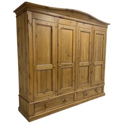Large pine quadruple wardrobe, the arched pediment over four panelled doors, the base fitted with two long drawers