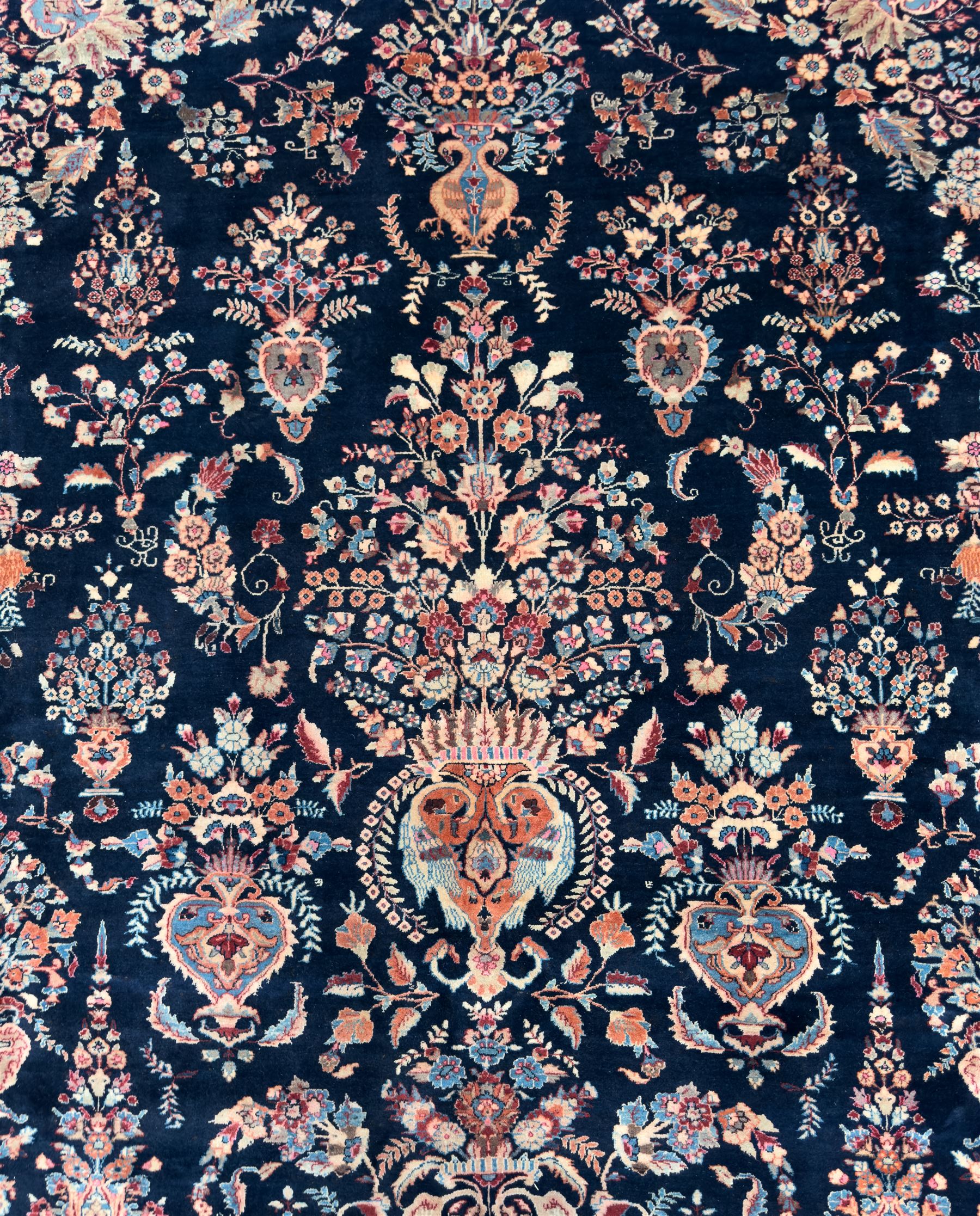 Northeastern Persian Meshed carpet, the deep navy field with a symmetrical floral arrangement of stylised flowerheads, palmettes and scrolling vines issuing from a central urn, enclosed by broad rust and blue borders of floral arabesques and lotus forms, from the region of Meshed