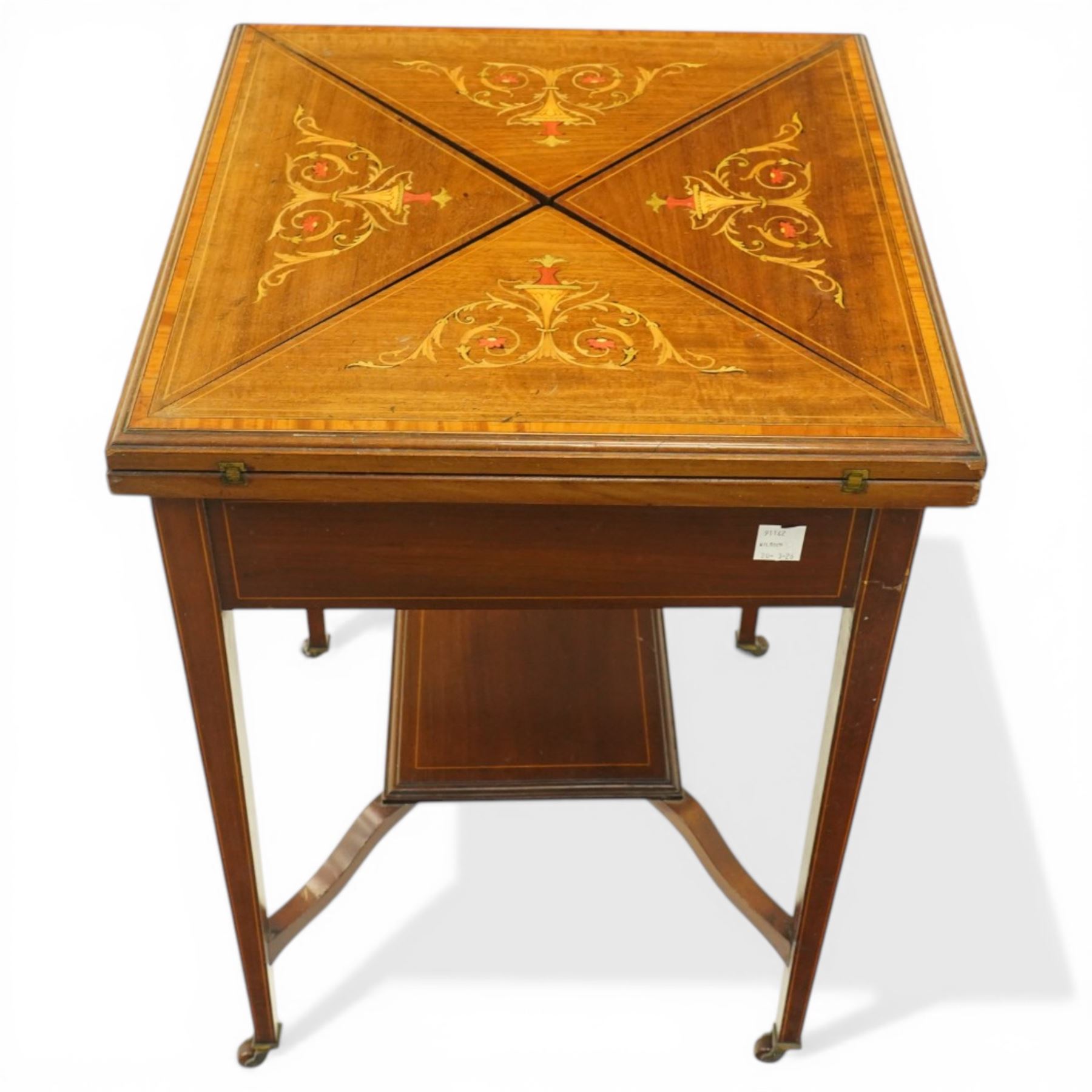 Edwardian inlaid mahogany envelope table, square top with triangular leaves revealing a baized lined interior and wells, raised on tapering supports united by an under tier, terminating in brass castors