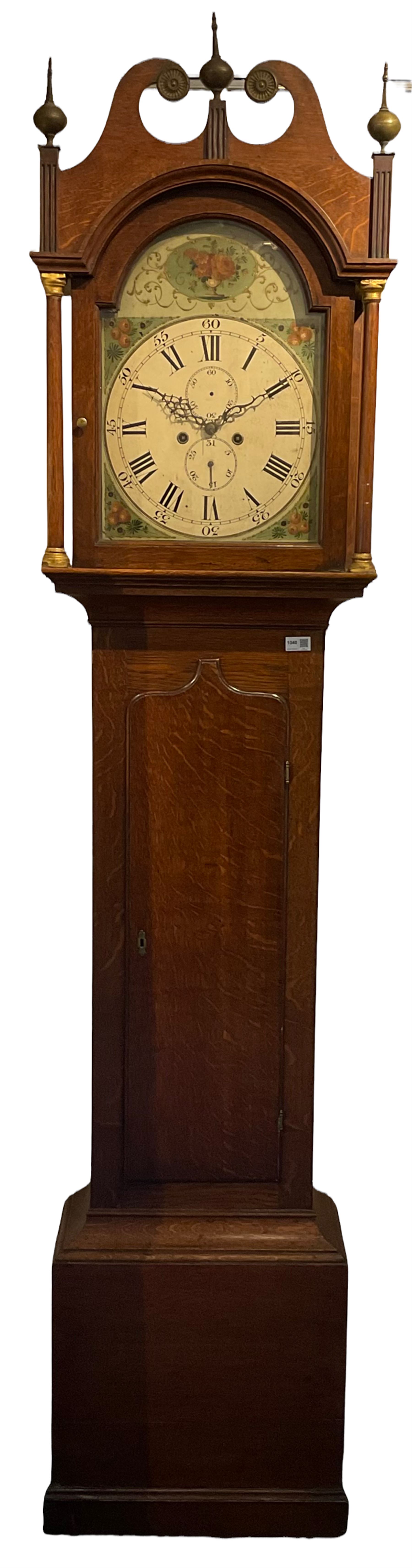 English oak cased longcase clock c1830, tall swan neck pediment with three ball and spire finals and brass paterae, break arch hood door flanked by two tapered columns with gesso capitals, with a slim trunk and full length door with a decorative ogee spire, on a square plinth with applied skirting, painted break-arch dial with depictions of flowers to the spandrels and break arch, spandrels and arch with raised gesso detailing on a green background, dial with Roman numerals and five-minute Arabic's, minute track, subsidiary date and seconds dial, with steel hands and calendar pointer (no second's hand), dial pinned via a cast falseplate to an eight-day rack striking movement, striking the hours on a bell. With weights,  pendulum and key.

