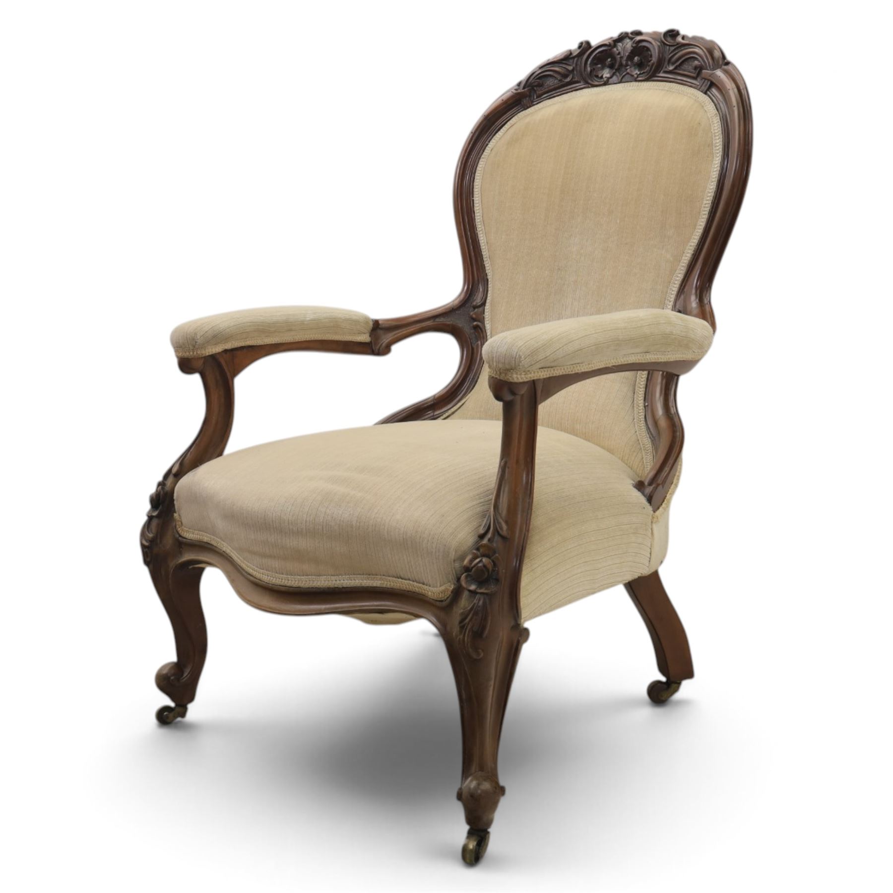 Late Victorian walnut open armchair, the carved shaped cresting rail centred by scrolls and foliage above a padded serpentine back and overstuffed seat upholstered in cream striped fabric, with padded scroll arms on open carved supports, raised on cabriole supports with carved knees and ceramic castors