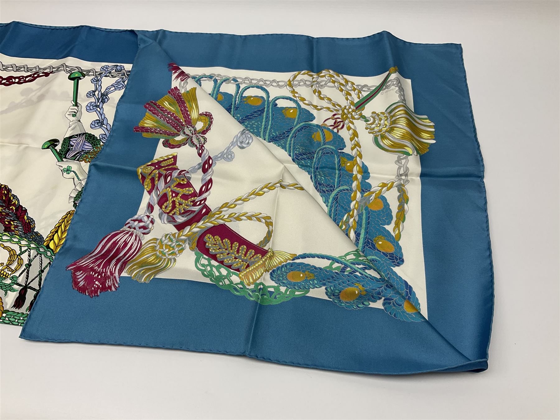 Hermès 'Le Timbalier' silk scarf, designed by Francoise Heron in 1961, printed with a central image of a gentleman on horseback donning extravagant dress, on white ground surrounded with colourful stylised knotted ropes, contained within peacock blue border, with rolled hand stitched edges and Hermes material label, 87cm square