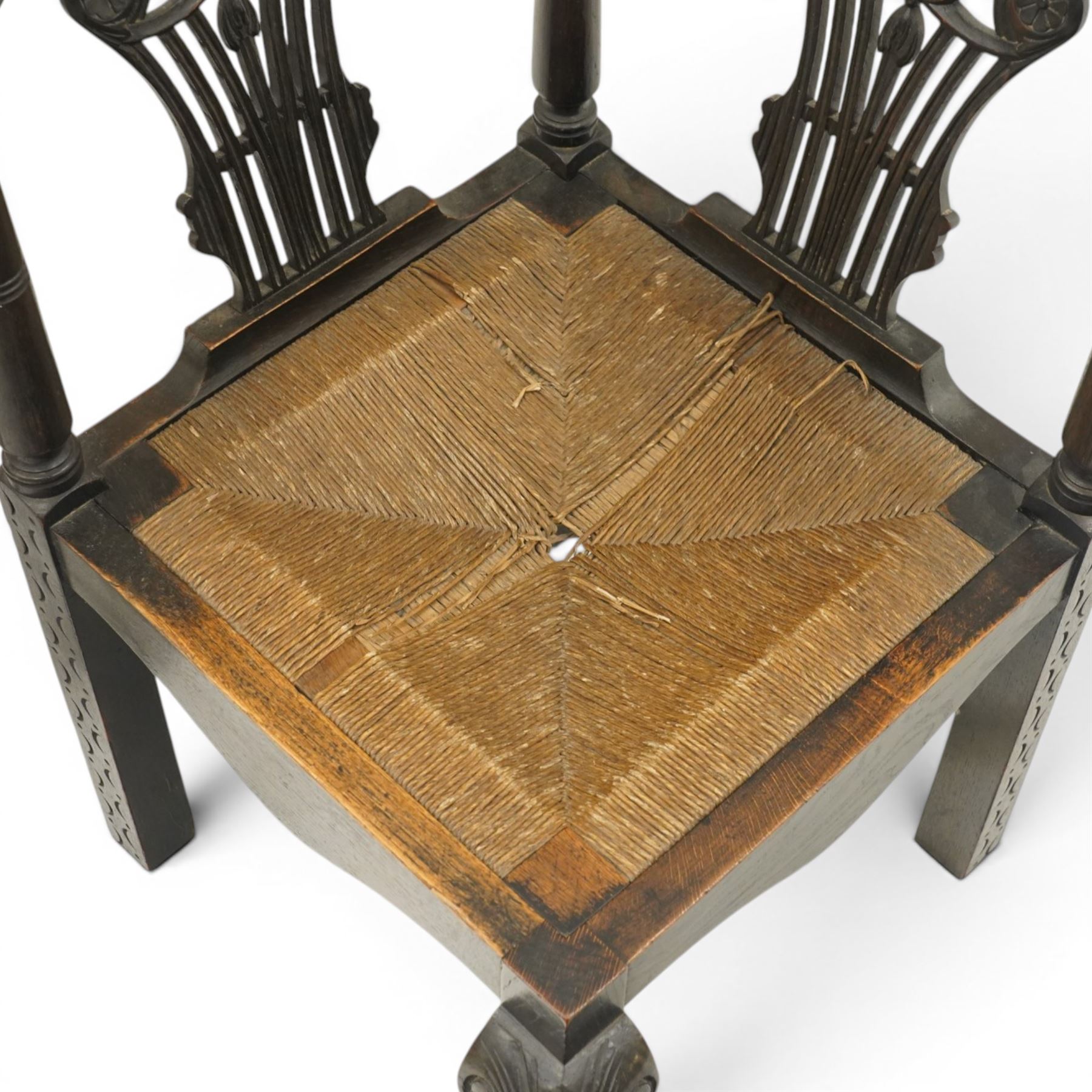 Pair of 19th century carved oak corner chairs, cresting rail carved with central floral bouquet with trailing foliage extending to the scroll arm terminals, pierced back splats with rosette motifs over drop-in rush seats, front cabriole support with acanthus carved knee and ball-and-claw foot