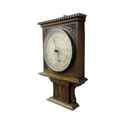 Edwardian - oak cased Arts and Crafts aneroid barometer with an 8” register, carved case with a flat top and dentil moulding, carved spandrels and carved plinth beneath, chrome bezel and flat bevelled glass (cracked)  steel indicating hand and brass recording hand, geometrically engraved dial centre, with an Arts & Crafts capitalized font, recording and indicating barometric pressure from 27 to 31 inches, with predictions.