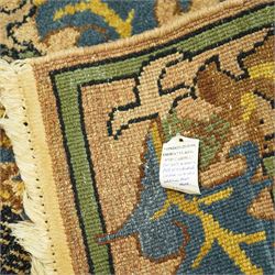 Arts & Crafts design wool pile rug, decorated with repeating stylized floral seed-head motifs and scrolling foliage within a complementary floral border in a muted palette of green, ochre, blue, and brown, with cotton fringe ends, with label for London House Oriental Rugs & Carpets  
