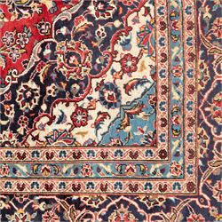 Persian Ardakan carpet, brick red field with ivory and navy central medallion, surrounded by stylised lotus blossoms and cloudband motifs, framed by rich indigo borders featuring palmettes, serrated leaves and angular vine work, woven in the city of Ardakan in central Iran