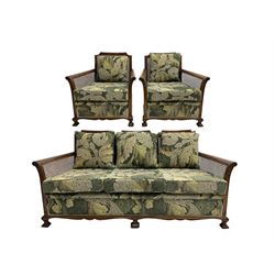 Early 20th century bergère lounge suite, mahogany framed with cane work back and sides, acanthus scroll carved uprights - three seat sofa (W167cm, H82cm, D83cm), and pair matching armchairs (W78cm), loose cushions upholstered in acanthus leaf scroll fabric with scatter cushions