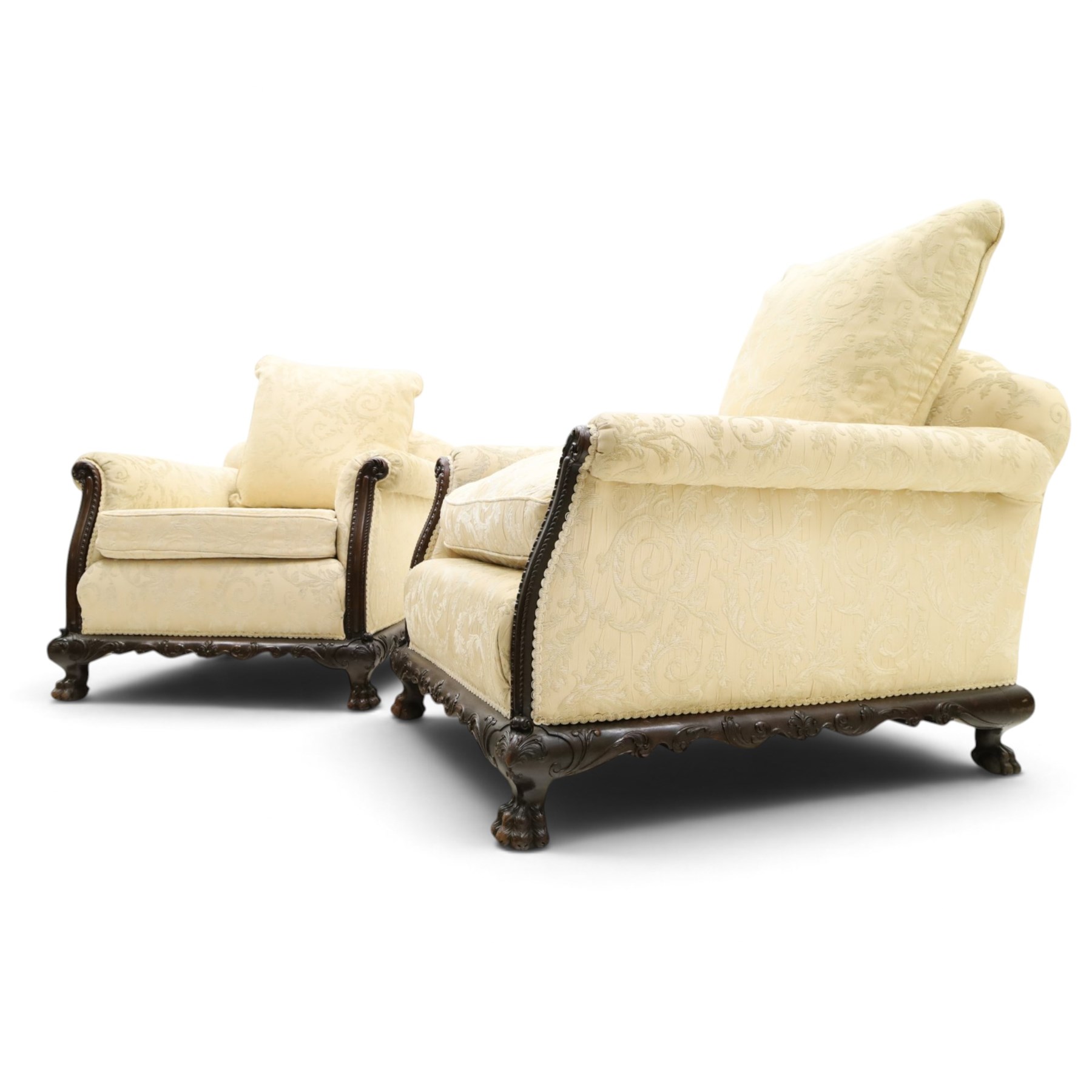 Quality Edwardian carved mahogany lounge suite comprising three-seater settee and pair of armchairs, the sofa with arched back over rolled arms and deep sprung seat, the arm terminals carved with acanthus rosette over gadroon and rope-twist moulding, the shaped apron carved and moulded with scrolling foliate acanthus motifs, terminating to four large front hairy paw and ball feet, upholstered in pale yellow foliate fabric with matching seat and scatter cushions (W200cm D105cm H73cm); the matching deep armchairs (W78cm D95cm H75cm)