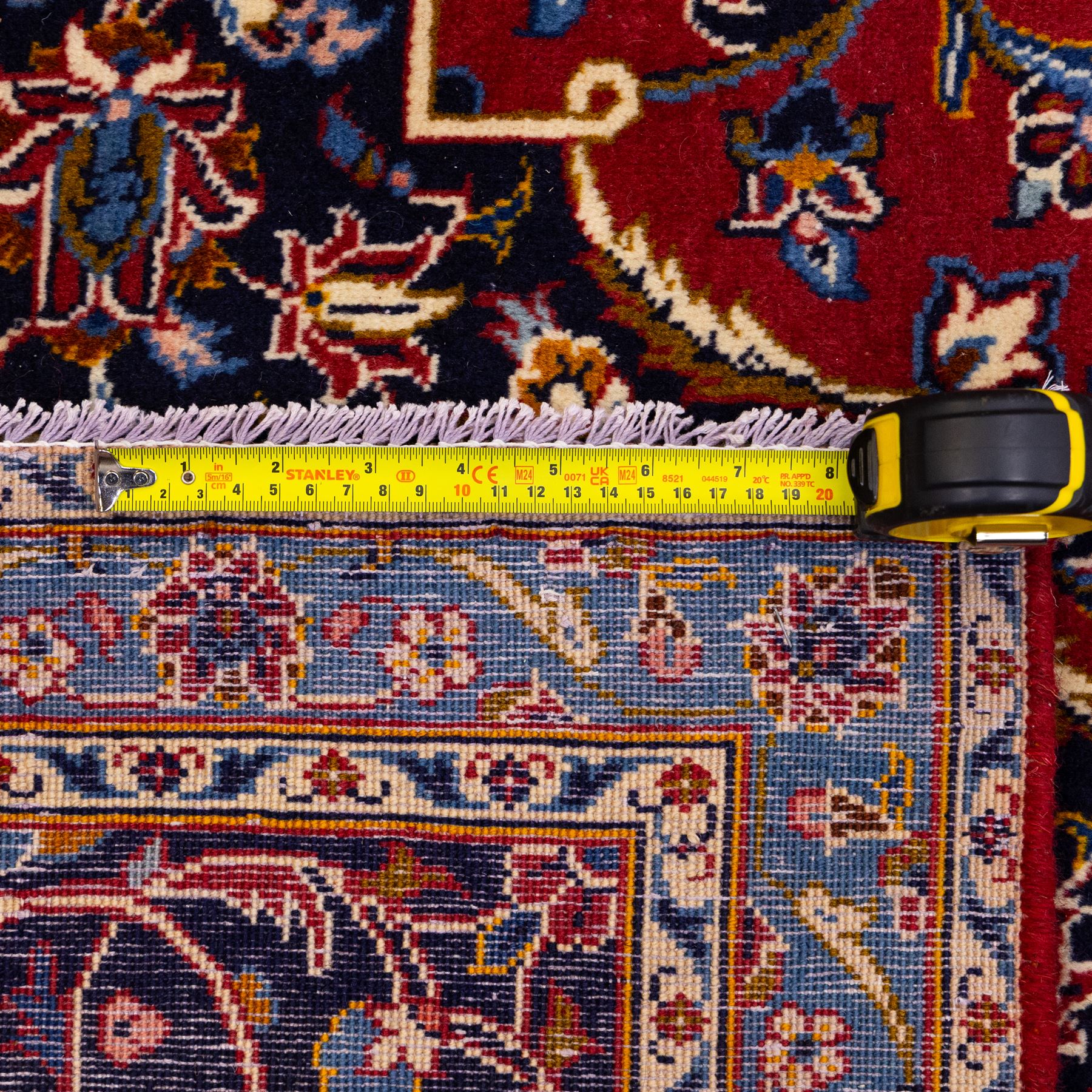 Central Persian Kashan hand-knotted carpet, rich crimson red field with a central cusped medallion with finely drawn floral sprays surrounded by dense scrolling vine work and palmettes, framed by a broad indigo ground border of flowering arabesques flanked by multiple guard stripes, in a palette of red, blue, ivory, sage green, and soft ochre tones, with cotton fringe ends    