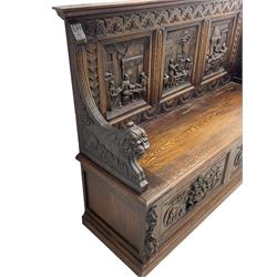 19th century heavily carved oak settle, the moulded upper rail over triangular foliage carved frieze, three Flemish style carved panels depicting tavern scenes, acanthus carved uprights terminating to lion carved arms, hinged box seat, the panelled front carved with lion masks and extending scrolled acanthus leaves, on moulded skirt base