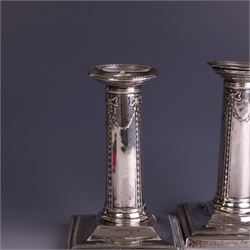 Pair of late Victorian silver mounted candlesticks, the stems embossed with classical ribbon and swag design, upon weighted stepped square bases, hallmarked London 1899, maker's mark worn and indistinct, H12cm
