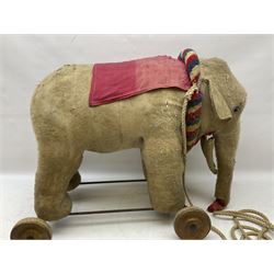 Early 20th century, plush straw filled pull along elephant, with red cloth and wooden wheels, H55cm 