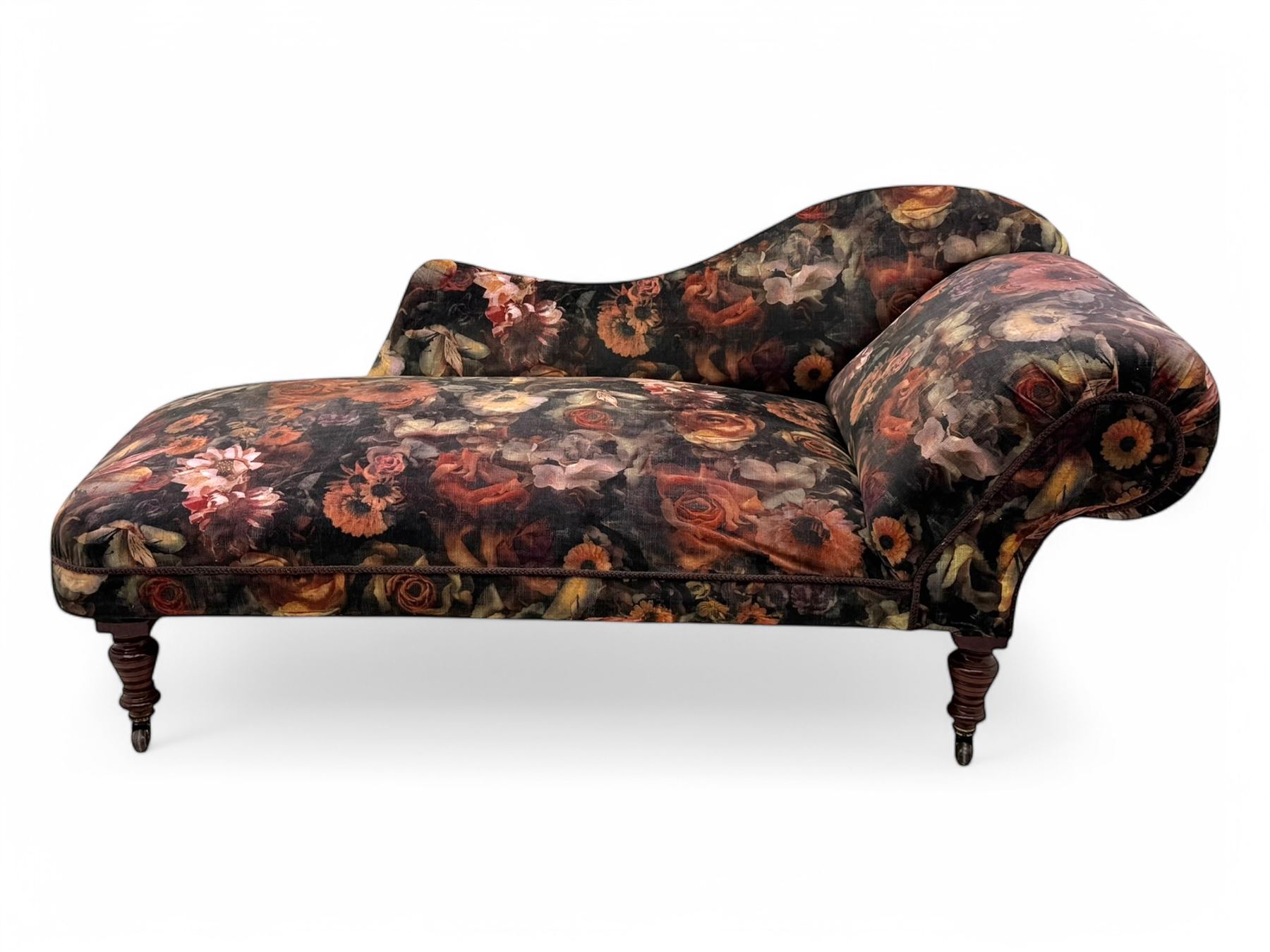 Victorian hardwood-framed chaise longue, serpentine back with rolled arm, upholstered in floral pattern fabric, on ring turned legs with ceramic castors 