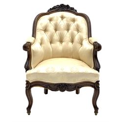 Victorian rosewood armchair, the shaped cresting rail carved with flowers and foliage, moulded frame, upholstered in buttoned cream patterned fabric, scrolled arm terminals and supports, shaped apron carved with flower heads, cabriole supports with castors