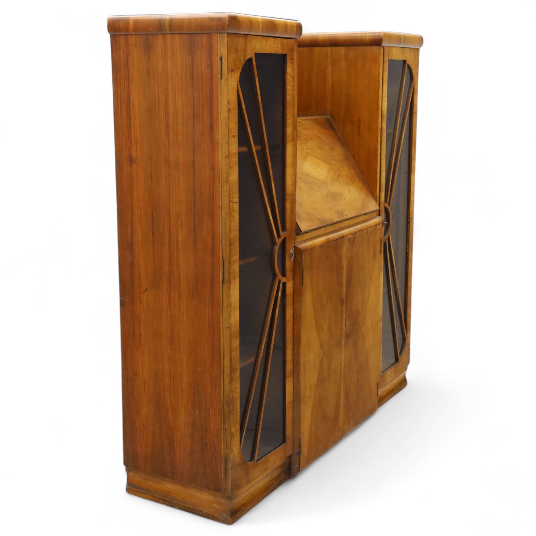 Art Deco walnut bureau bookcase, top with moulded and rounded edges and stepped front profile, central shelf, and fall-front bureau section with vertical and horizontal pigeon holes and a small drawer, above two cupboard doors and flanked by two tall glazed display cabinets with single doors and geometric sunburst design astragal glazing bars enclosing three shelves, raised on cavetto shaped plinth base 