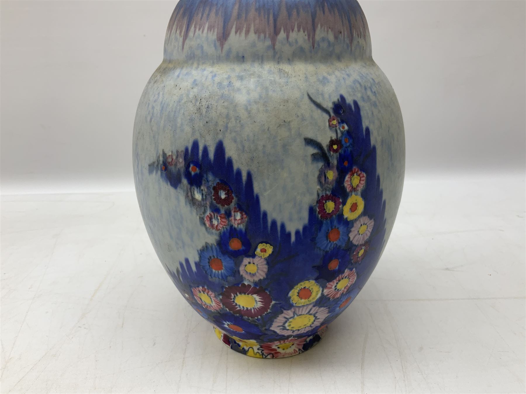 1930s Carlton Ware Art Deco Garden pattern vase of shouldered ovoid form, decorated with blue, pink and yellow flower heads on a mottled blue and white ground, pattern no. 3413, with printed and painted marks beneath, H19cm, together with a Clarice Cliff My Garden pattern vase, raised upon three feet with blue, pink and purple moulded Hollyhock design, H20cm, with Clarice Cliff Wilkinson Ltd England marks beneath