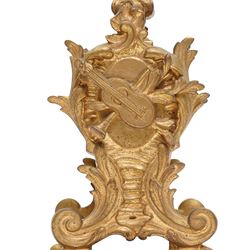 French-Late 19th century 8-day gilt brass rococo style mantel clock, c1890, waisted case  decorated with scroll work, leaves and musical instruments, resting on an attached plinth with splayed feet, dial within a glazed brass bezel with a gilt repoussé centre, porcelain cartouche Roman numerals and steel fleur-di-Lis hands, with a twin train movement, recoil anchor escapement and countwheel strike, sounding the hours and half-hours on a bell. With a matching pair of five-light candelabra. No Pendulum or Key.
