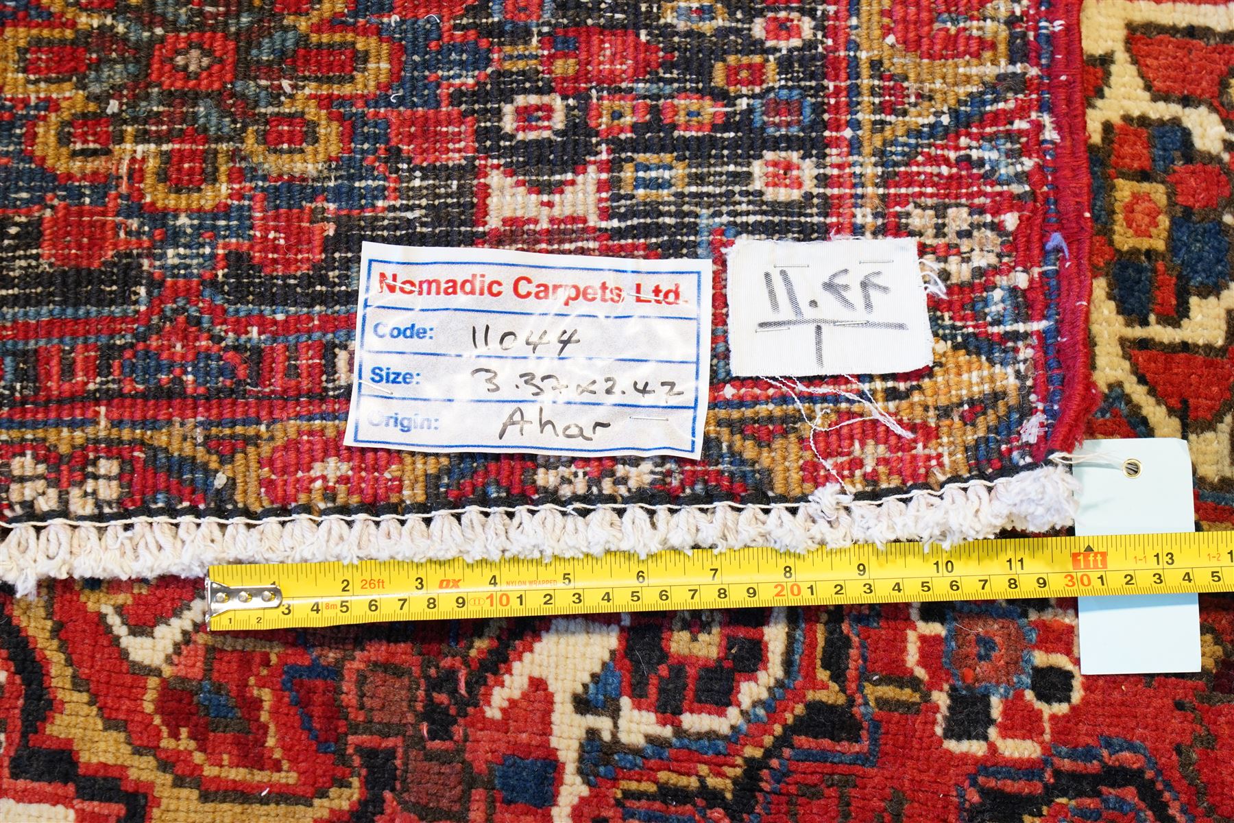 North West Persian Heriz/Ahar hand-knotted carpet, brick-red field with a large central angular stepped medallion with pendant motifs, surrounded by stylized palmettes, serrated leaves and geometric floral devices , ivory corner spandrels, enclosed by a dark indigo main border of stylized rosettes and angular vine motifs, between multiple guard stripes, with cotton fringe ends 