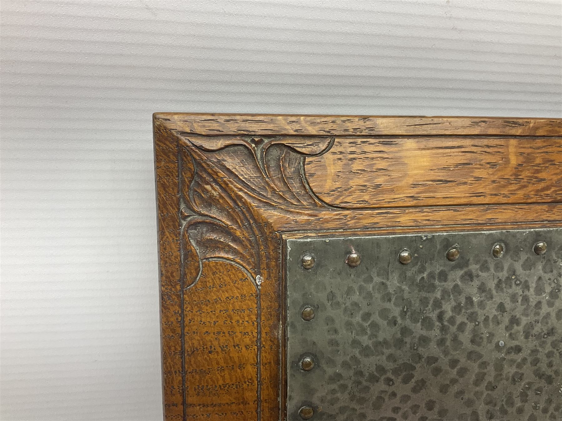 Arts and Crafts oak stand by Arthur Simpson of Kendal, of rectangular form with central hammered pewter panel, surrounded by a border with carved foliate corners, upon two bar supports, bearing label detailed 