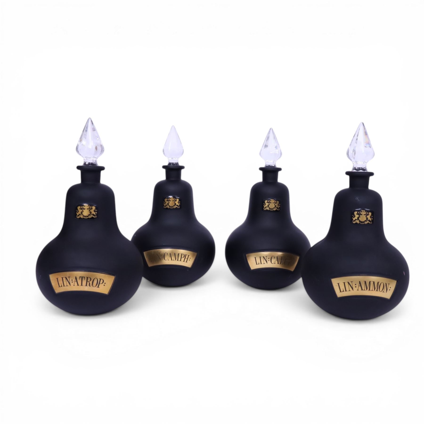 Set of four 20th century Royal Pharmaceutical Society black frosted glass bottles, of bellied form with clear cut glass spire stopper, each body bearing gilt label in Latin: LIN:AMMON:, LIN:ATROP:, LIN:CAMPH:, and LIN:CALCi:, and gilt Royal Pharmaceutical Society crest to neck, H25cm

Provenance: From the collection of the family of Peter Green, a practising pharmacist whose career spanned the mid to late 20th century. During his professional life he managed pharmacies in Yeovil, Somerset, and later Selles Chemist in Filey, North Yorkshire, before purchasing and running his own business, Peter Green Pharmacy, located in the Market Place, Malton. The bottles were displayed as part of the traditional shop fittings in both the Filey and Malton pharmacies and were retained as part of his collection.