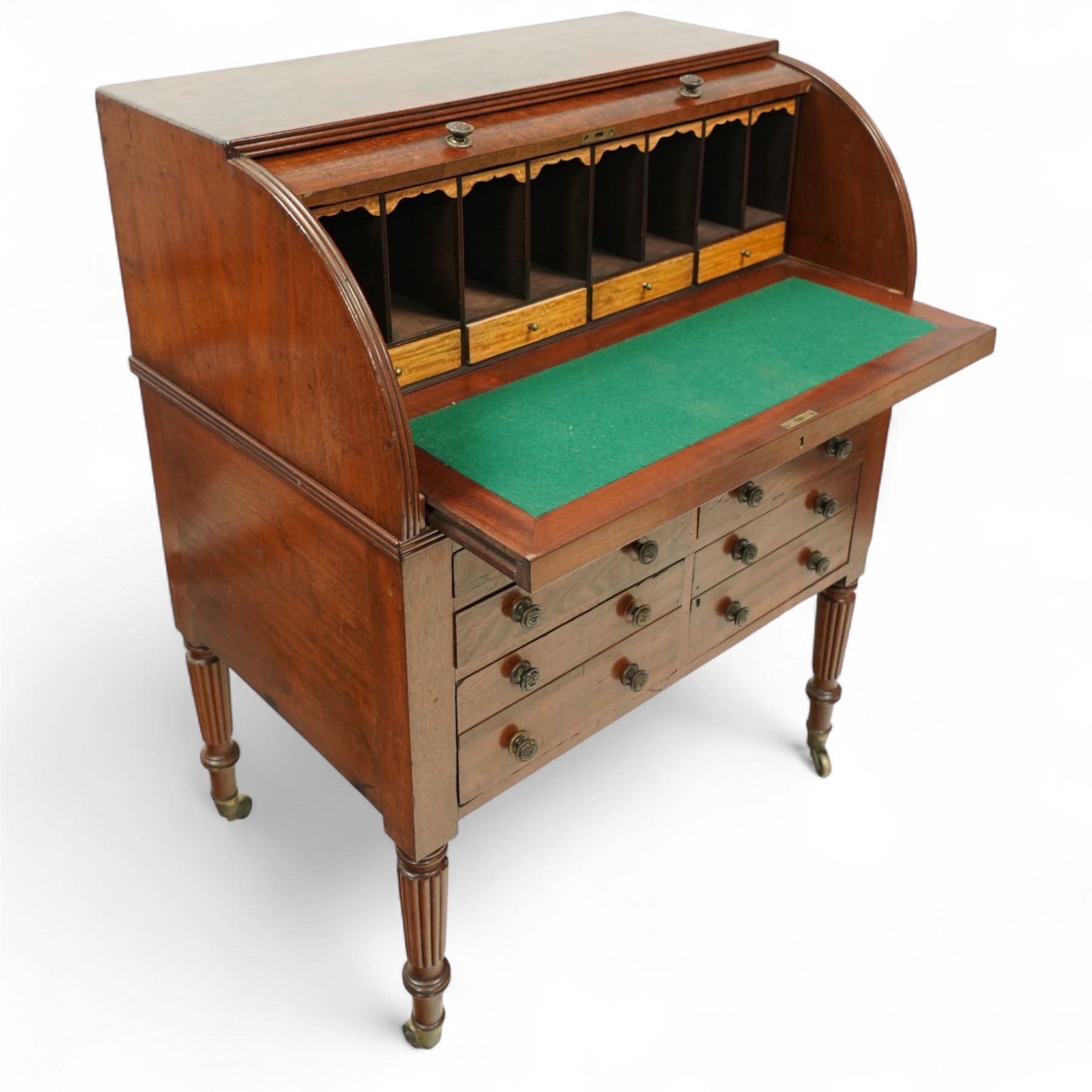 Regency period mahogany cylinder desk, the roll-top enclosing a fitted satinwood interior with pigeonholes and drawers, sliding green baize writing surface, lower section fitted with four drawers and a cupboard, on reeded tapering legs with brass caps and castors