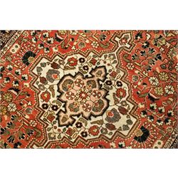 Persian Heriz-style rug, bold geometric octagonal medallion, rich red field with ivory spandrels, dark navy border, rosettes and vines; inner guards with repeating patterns 