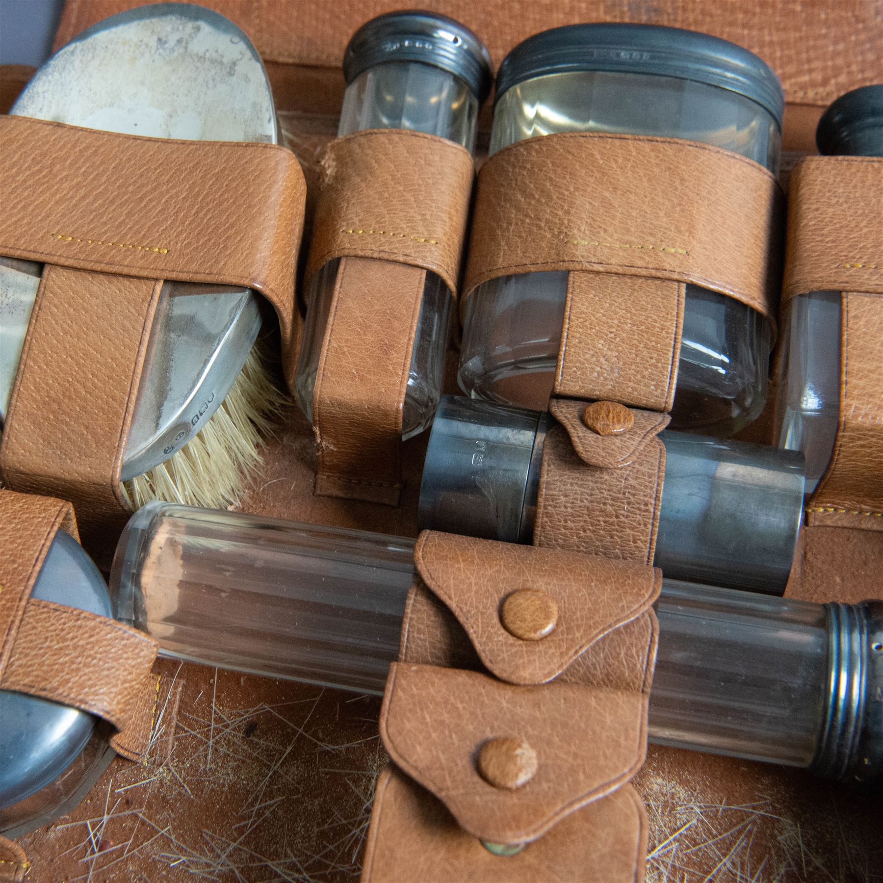 1920s gentleman's travelling case by Mappin & Webb Ltd, tan leather impressed with initials NAO, opening to reveal a compartmentalised interior containing silver mounted dressing table items, including a pair of silver mounted brushes, engraved NAO AMA 1918, hallmarked William Comyns, London 1911, five faceted glass jars and bottles with silver lids and a silver shaving brush holder, all hallmarked Mappin & Webb Ltd, London 1922, tan leather box containing razor, silver plated shoe horn, scissors and bevelled edge shaving mirror with easel support