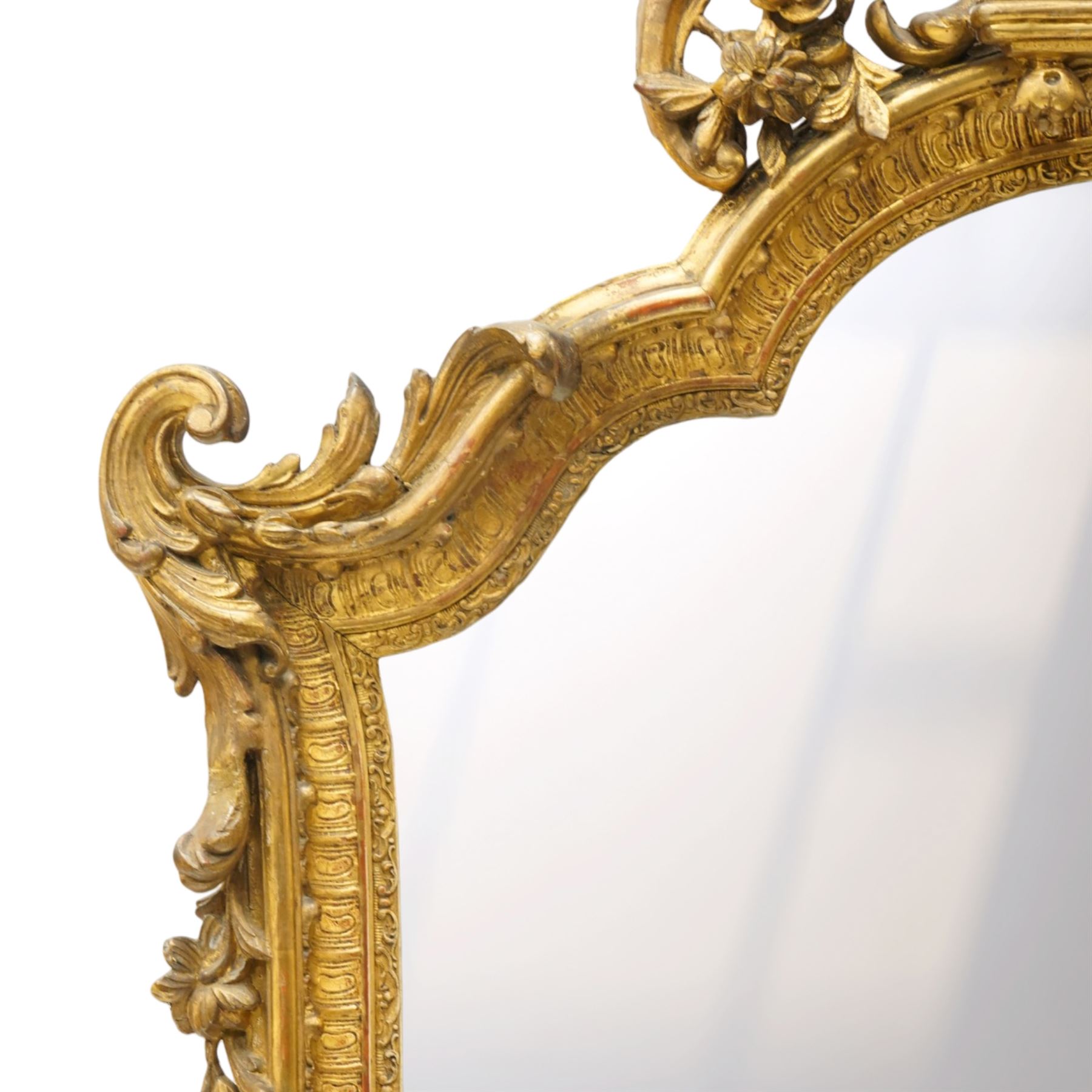 Victorian giltwood and gesso framed ornate wall mirror, the protruding cartouche pediment decorated with extending scrolls of acanthi and flower heads, with scrolled foliage corners flanking a carved slip with further gadrooned scroll decoration, contained a shaped rectangular bevelled plate, over a pierced and scrolling scallop shell terminal