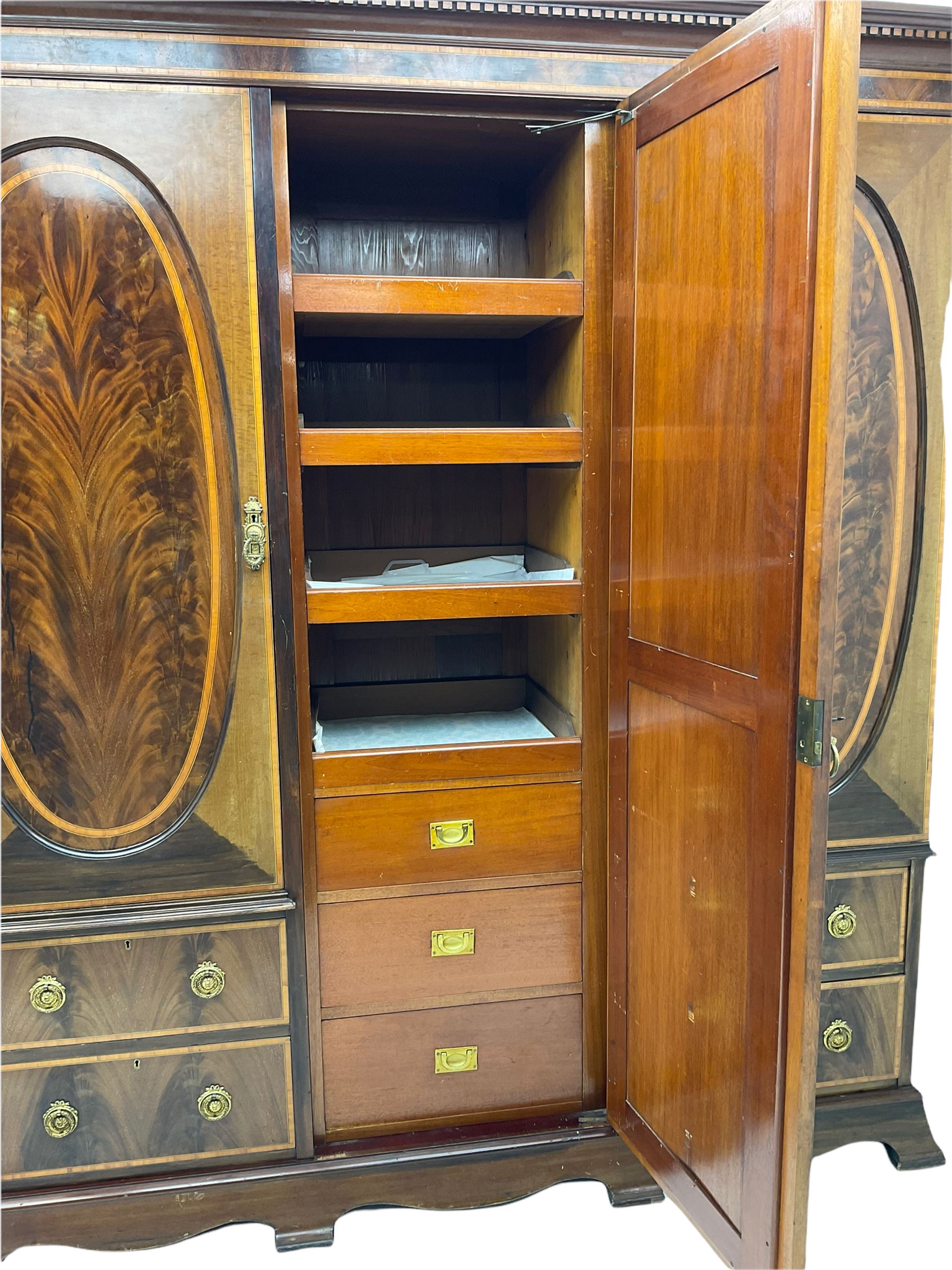 James Shoolbred & Co. London - Edwardian inlaid mahogany triple combination wardrobe, projecting dentil cornice over bevel glazed door, two figured oval panelled doors and four drawers, the central compartment fitted with linen slides and drawers, satinwood banding, on base with shaped apron and bracket feet, with enamel plaque 