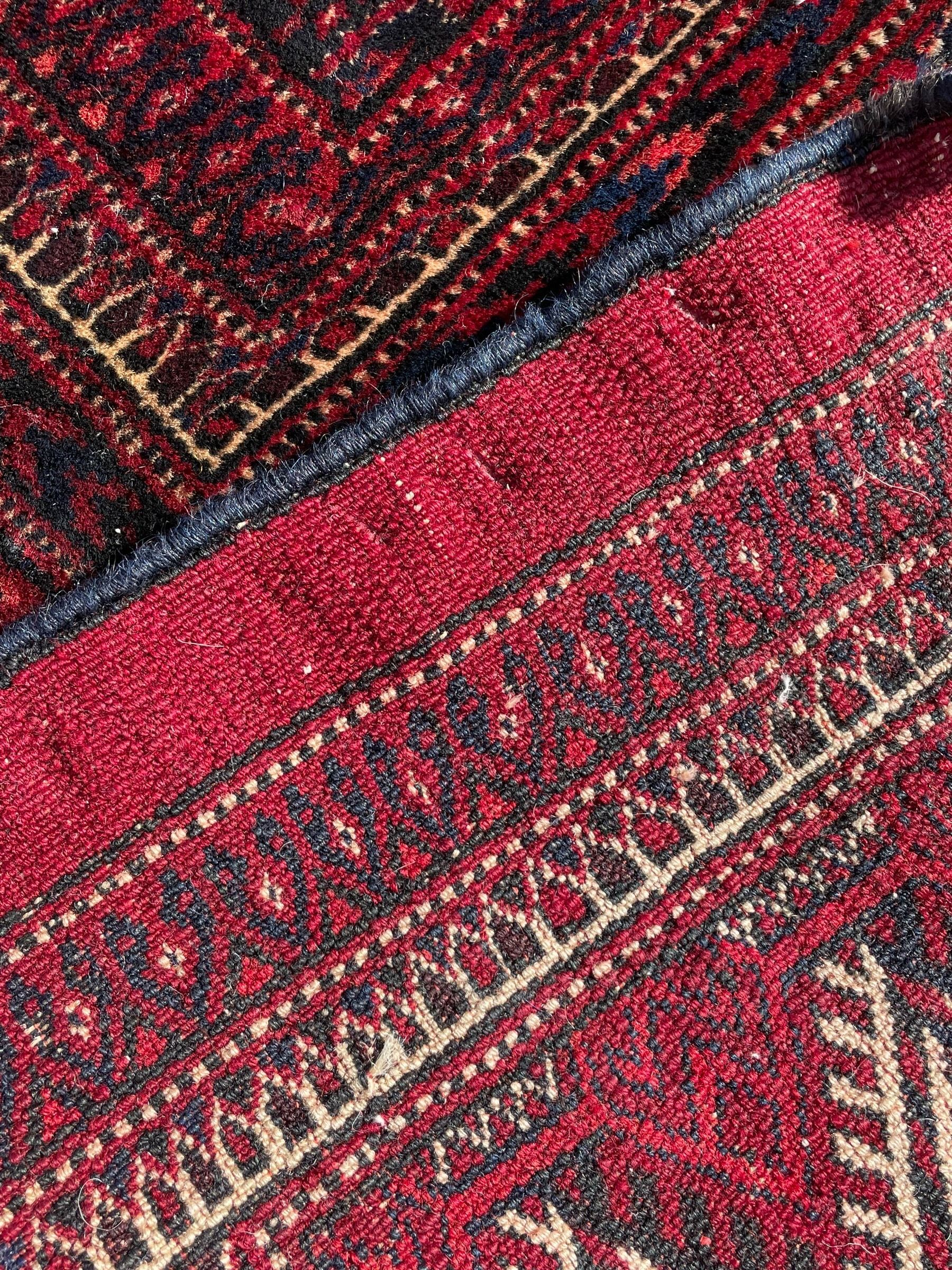 Afghan Bokhara red ground carpet, the field decorated with four rows of Gul motifs interspersed with Hac motifs, the border with lattice pattern panels within small geometric guard stripes, geometric patterned end panels