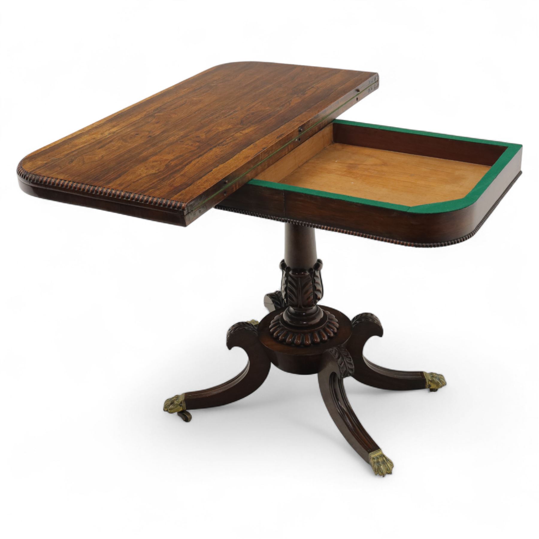 Regency rosewood fold over card table, the rectangular top with rounded corners and gadrooned edge opening to reveal a green baize lined interior, raised upon convex lobbed and acanthus pedestal and four fluted sabre legs, terminating in brass lion paw feet and castors