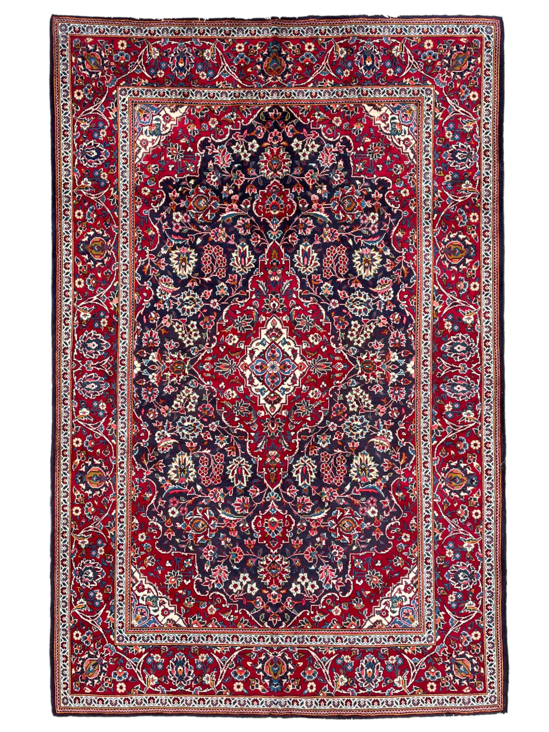 Persian indigo ground rug, the central crimson pole lozenge medallion surrounded by interlacing floral patterns, the main border with repeating plant motifs connected by scrolling branches