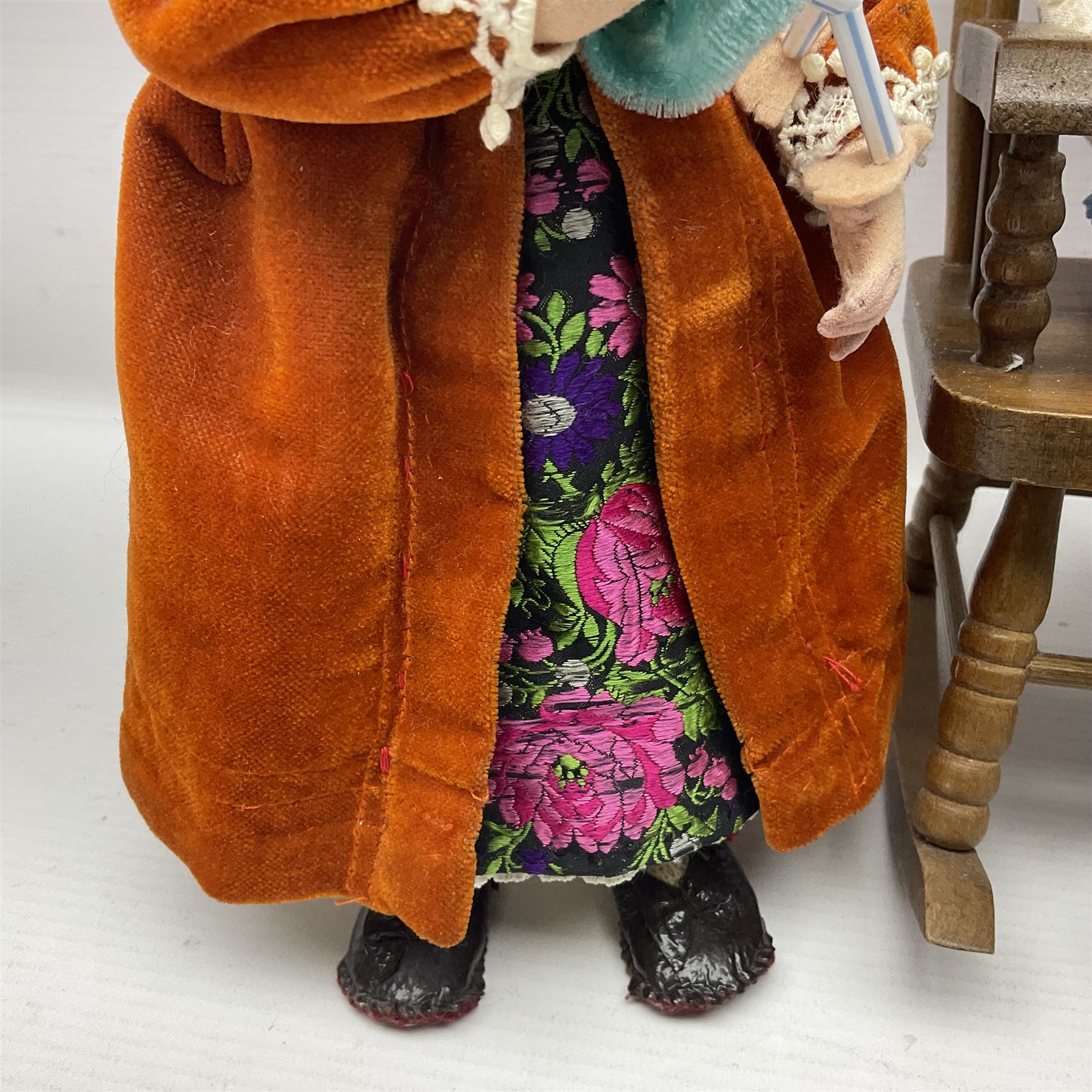 Anna Meszaros Hungary - three hand made needlework figurines - 'The Cobbler' as a child seated in a wooden rocking chair working on a removed boot H24cm; young girl standing crying holding a doll with broken head H32cm; and young girl in long dress and bonnet standing holding a doll H27cm (3)  Auctioneer's Note: Anna Meszaros came to England from her native Hungary in 1959 to marry an English businessman she met while demonstrating her art at the 1958 Brussels Exhibition. Shortly before she left for England she was awarded the title of Folk Artist Master by the Hungarian Government. Anna was a gifted painter of mainly portraits and sculptress before starting to make her figurines which are completely hand made and unique, each with a character and expression of its own. The hands, feet and face are sculptured by layering the material and pulling the features into place with needle and thread. She died in Hull in 1998.