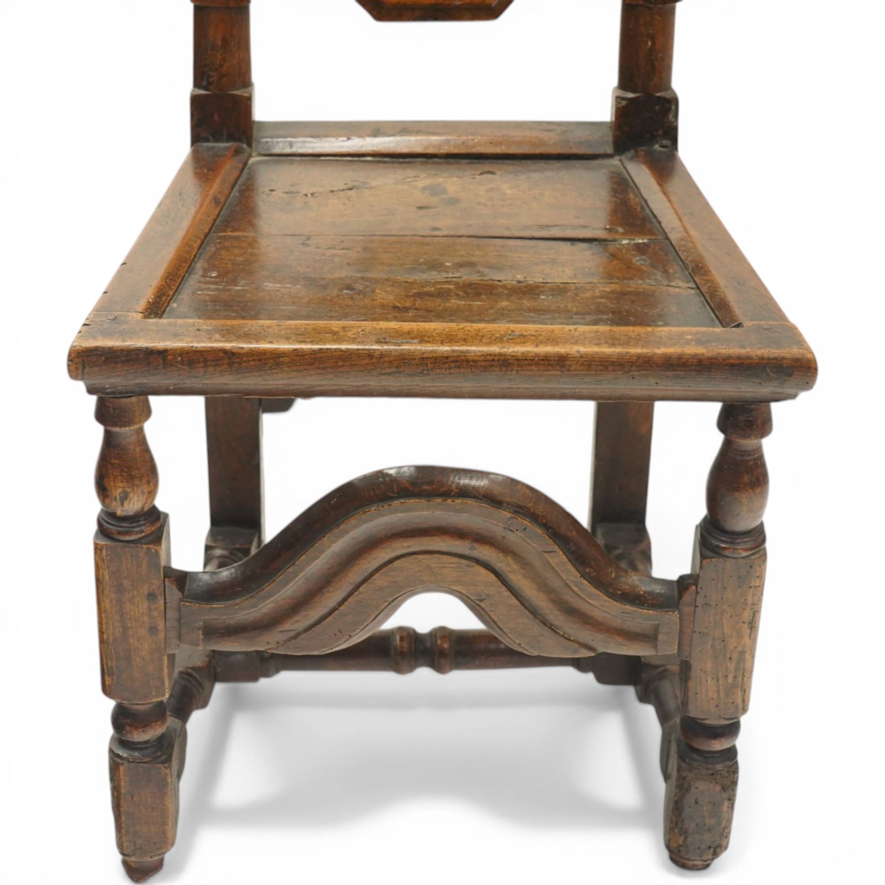 17th century oak and elm hall chair, the high-back with shield-shaped fielded panelling flanked by turned uprights, over a panelled seat, raised on turned supports united by H-stretcher with moulded serpentine front-stretcher