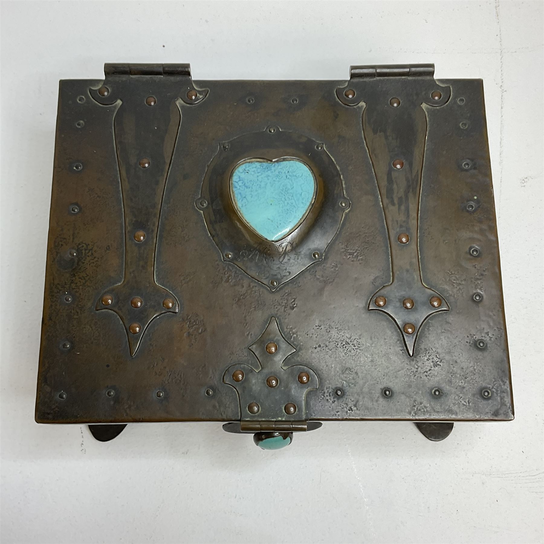 Arts and Crafts copper box, the lid decorated with stylised riveted hinges and inset with Ruskin type ceramic turquoise heart-shaped cabochon, the mount etched M.B 1913, and further cabochon roundel to each side panel, including one inset to the clasp acting as the knob to the locking mechanism, marked RS Douglas 1913 beneath, W16.5cm H7cm D15cm