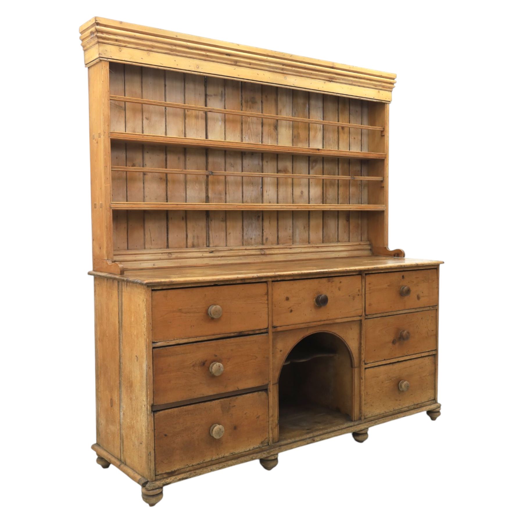 Early 19th century waxed pine farmhouse dresser and rack, the rack featuring two plate shelves and bars above seven drawer base with centre 'dog kennel' recess, raised on turned feet