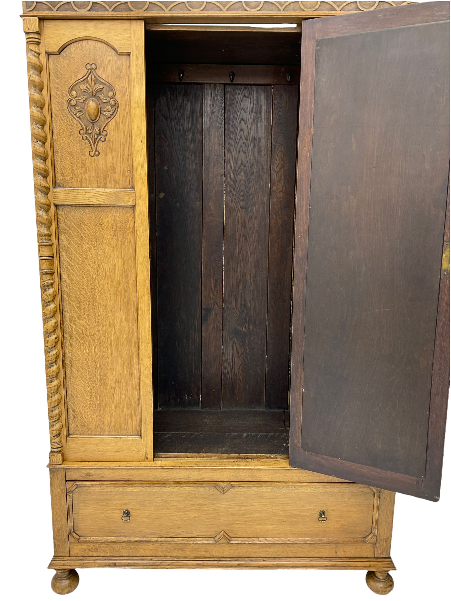 Early 20th century oak wardrobe, projecting cornice of blind fret-work frieze, oval bevel edge mirror door, half spiral turned pilasters, drawer to base with mouldings, on turned bun feet