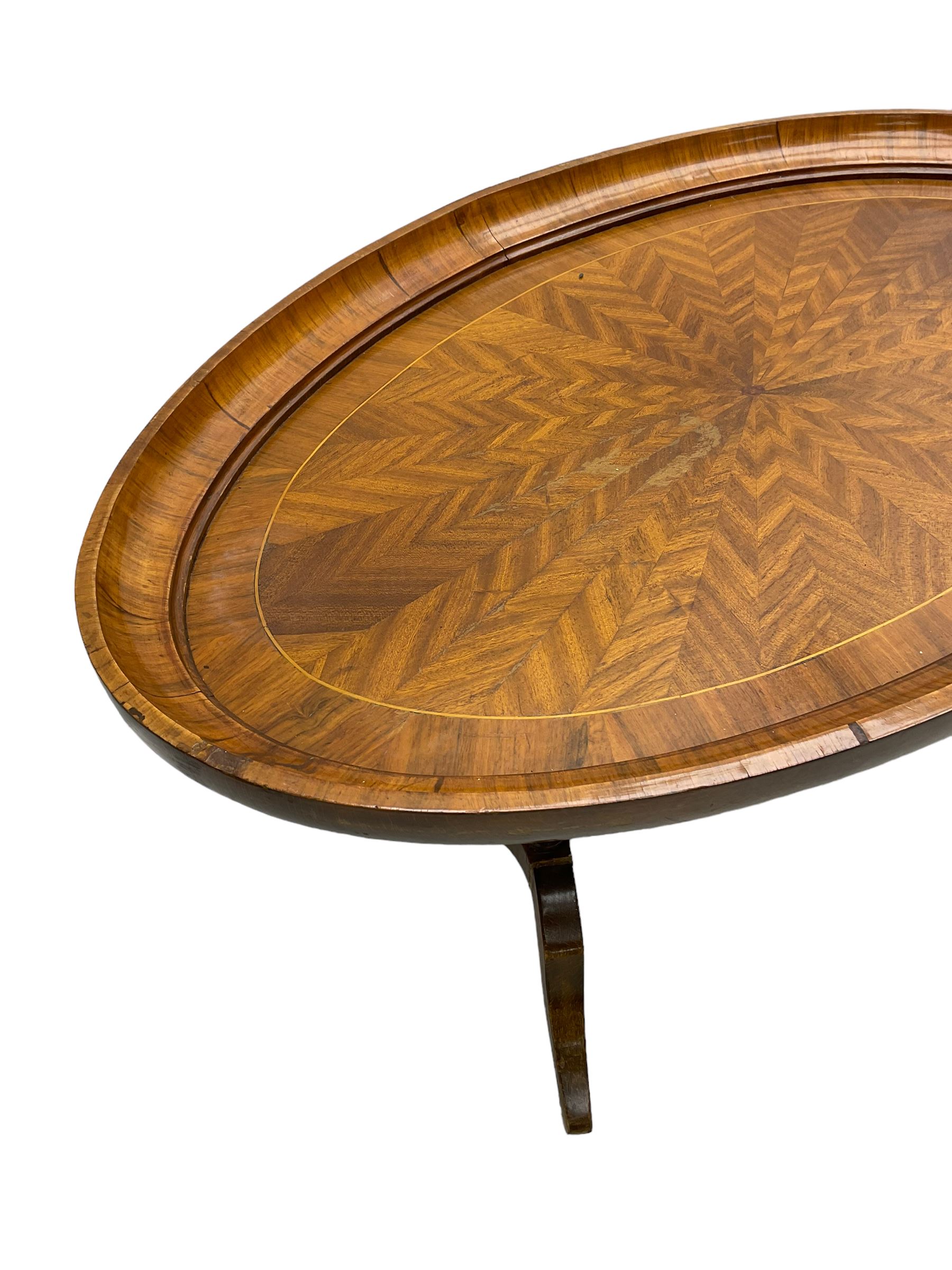 Early 20th century walnut coffee table, oval dished top with sunburst matched veneer, raised on twin cluster columns united by turned stretcher base on splayed supports