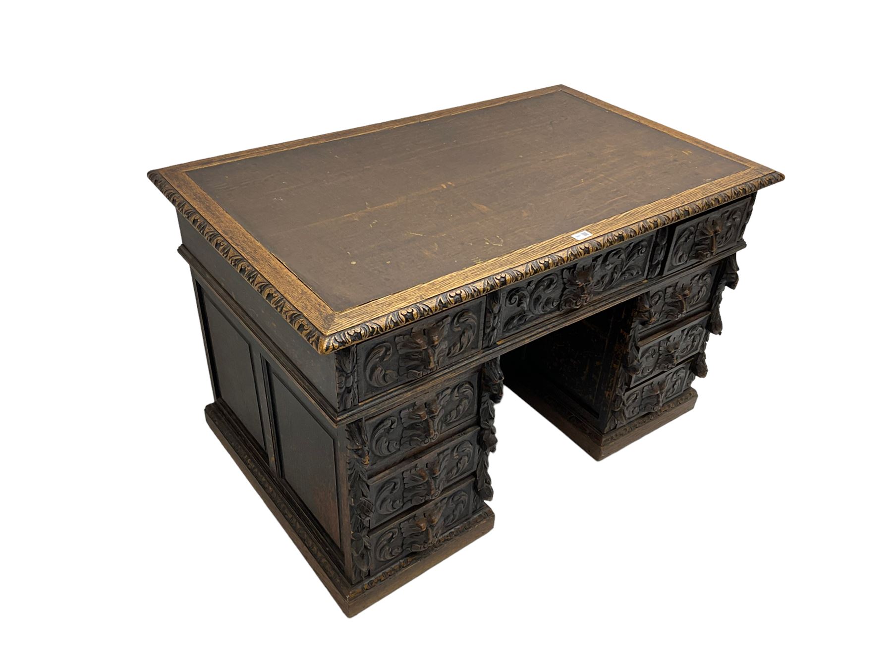 Late 19th century Gothic revival carved oak twin pedestal desk, rectangular top with inset writing surface and carved edges, central frieze drawer flanked by eight drawers, all with green man carved handles and extending trailing foliage, carvings of pineapple and lion mask corbels, the pedestals with panelled sides and back, on plinth bases