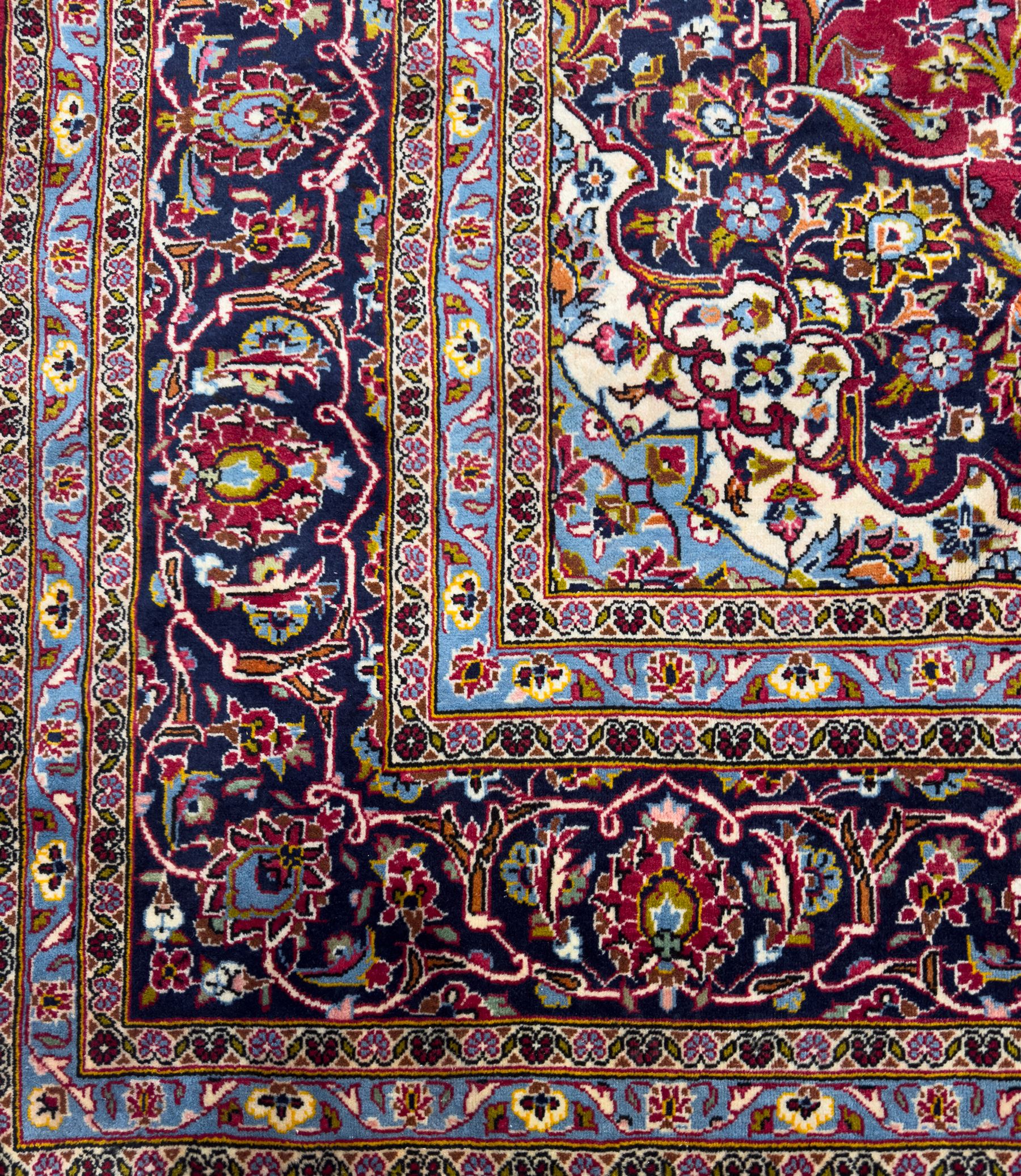 Central Persian Kashan hand-knotted carpet, the madder red field with central lobed medallion in indigo and ivory, enclosing scrolling arabesques and flowerheads, framed by palmette spandrels and an indigo border of rosettes and lotus forms between multiple floral guard stripes, from the region of Kashan