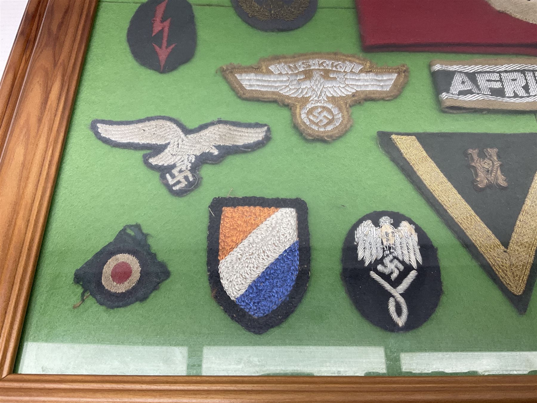 Framed display of thirty-four WWII German cloth badges including Luftwaffe pilot, Paratrooper, Afrikakorps cuff title, sleeve insignia for 'SS' Foreign Volunteers, various breast eagles including Luftwaffe, Army etc, RAD badges, Party Armband, rank and trade insignia, cap insignia etc; 40 x 50cm in modern pine frame
