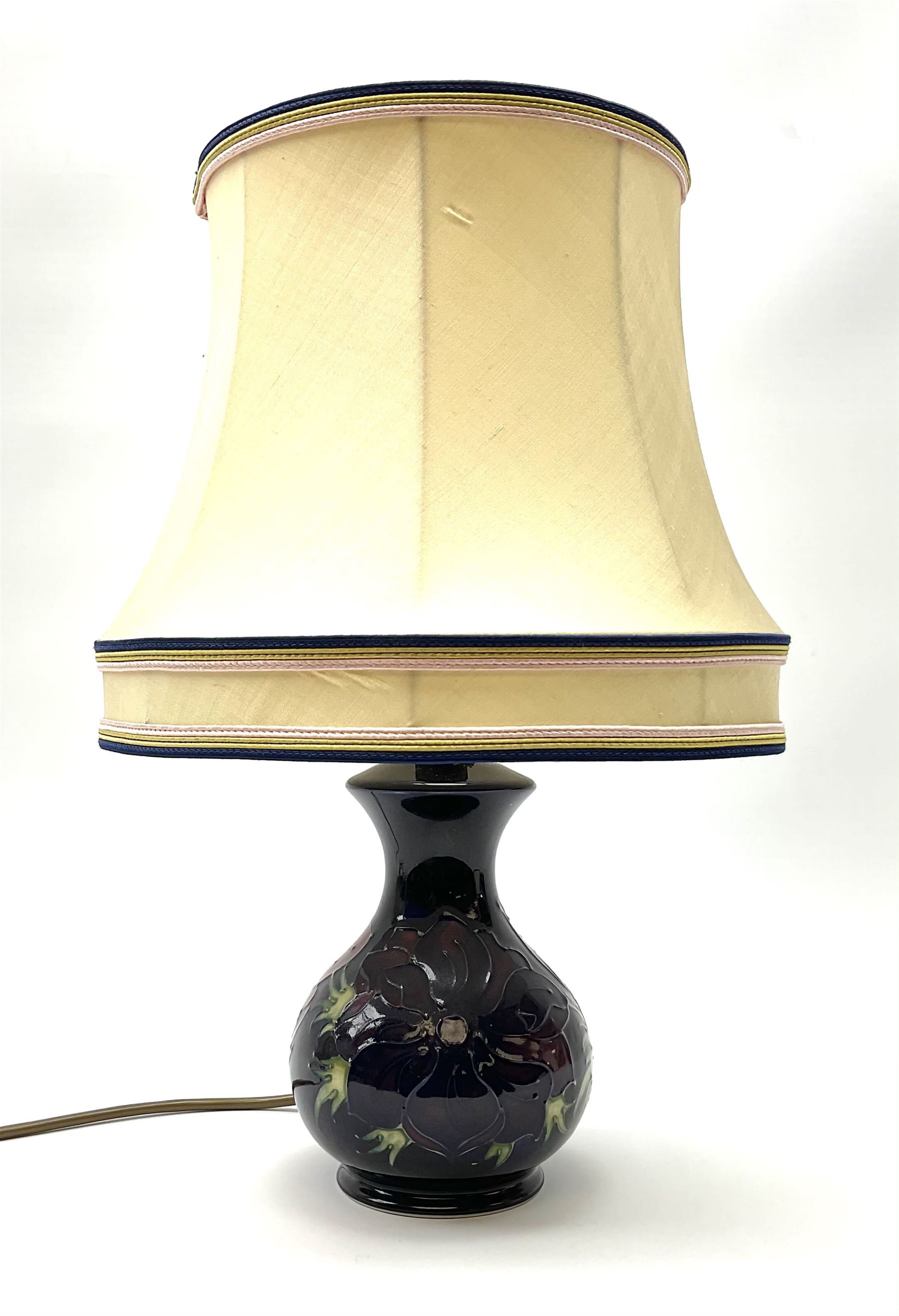A Moorcroft table lamp, of baluster form, decorated in the Anemone pattern upon a dark blue ground, with impressed marks beneath, with accompanying cream shade with piped detail, overall H38.5cm.