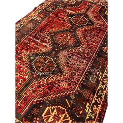 Persian Shiraz rug, red ground field decorated with linked triple lozenge medallions, decorated all over with stylised flower and plant motifs, geometric design triple band border