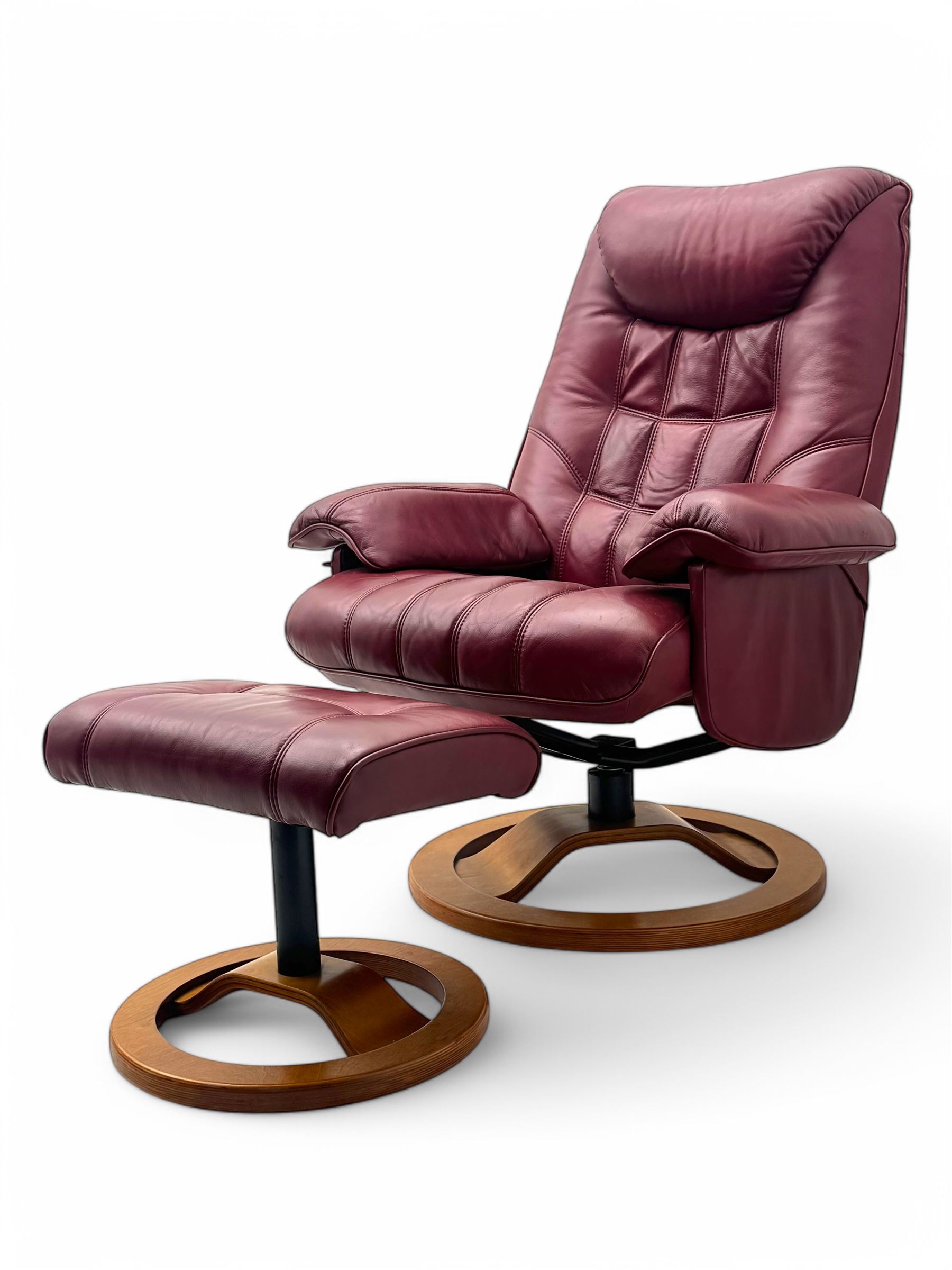 Contemporary burgundy leather reclining armchair and footstool, featuring segmented upholstered cushions and padded armrests, each piece mounted on a circular laminated wood base
