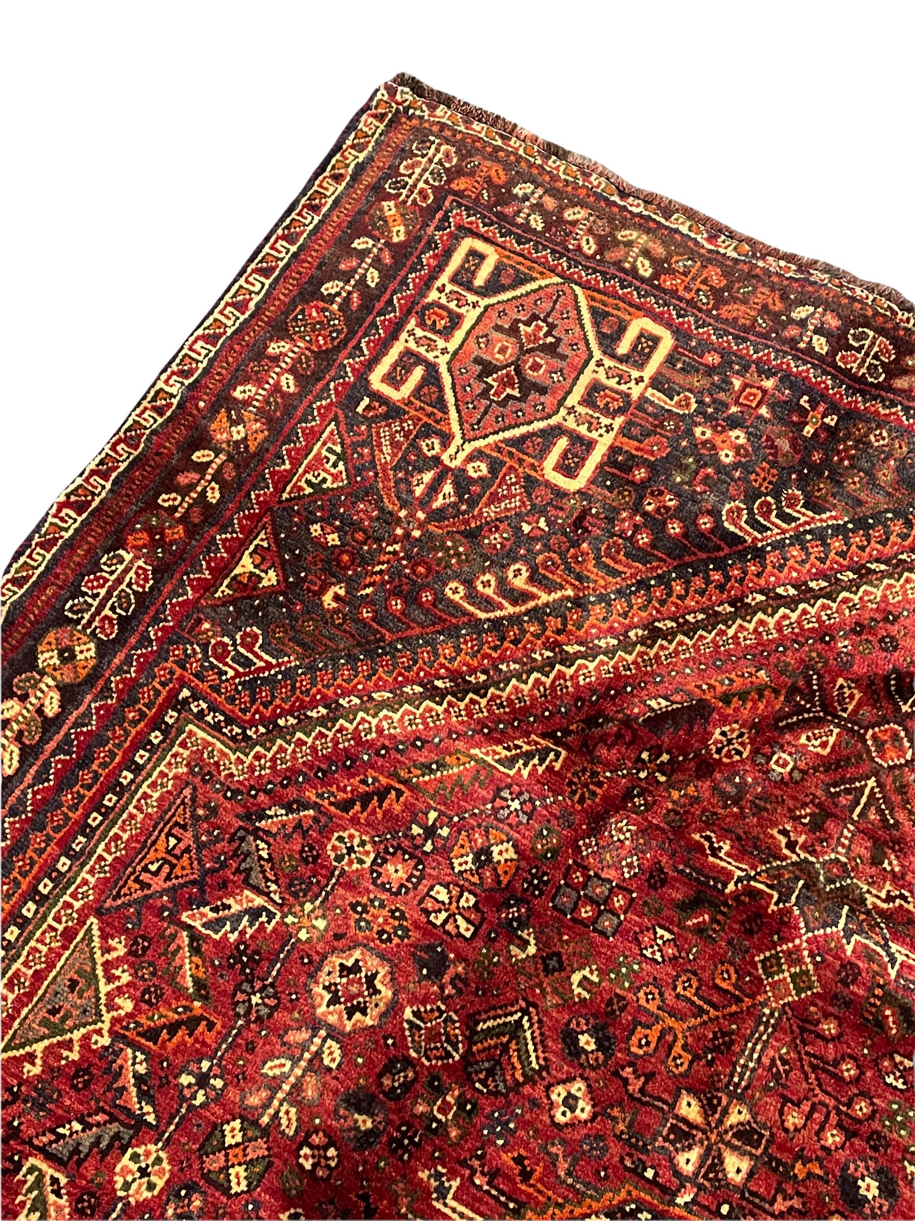 Persian Qashqai red ground rug, the main field decorated profusely with small stylised motifs, central lozenge medallion, multi-band border decorated with trailing foliate and flower head motifs 