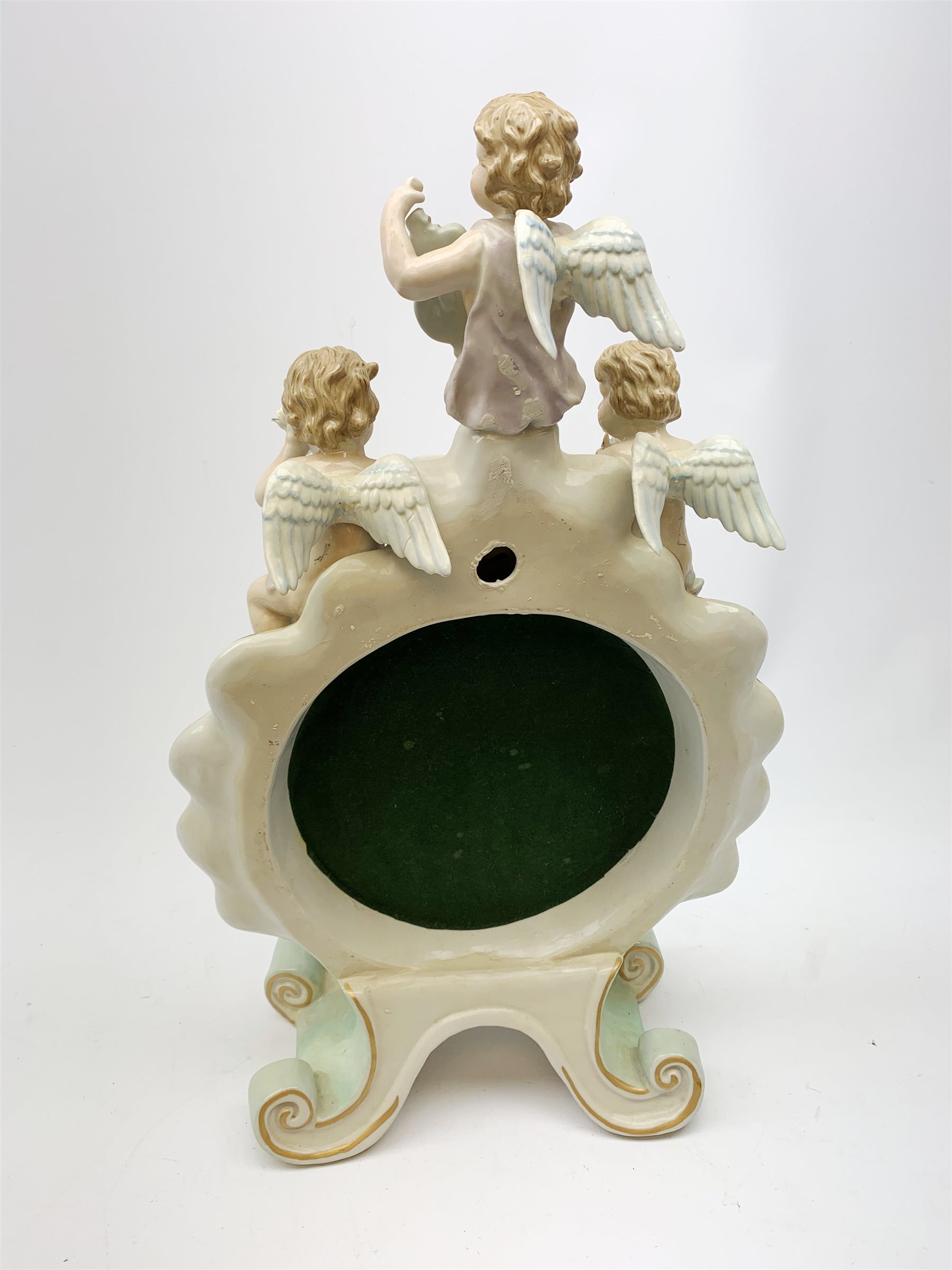  A late 19th century Sitzendorf porcelain mirror, the mirror plate of circular form set within a shaped surround encrusted with flowers and foliage, surmounted by three figures of cherubs and raised upon four scroll feet, with blue cross hatch mark beneath, H57cm.   