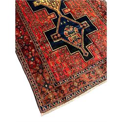 Persian Kurdish rug, red ground field decorated with small stylised motifs with triple linked medallions, three band border, the main band with scrolling design and decorated with floral motifs