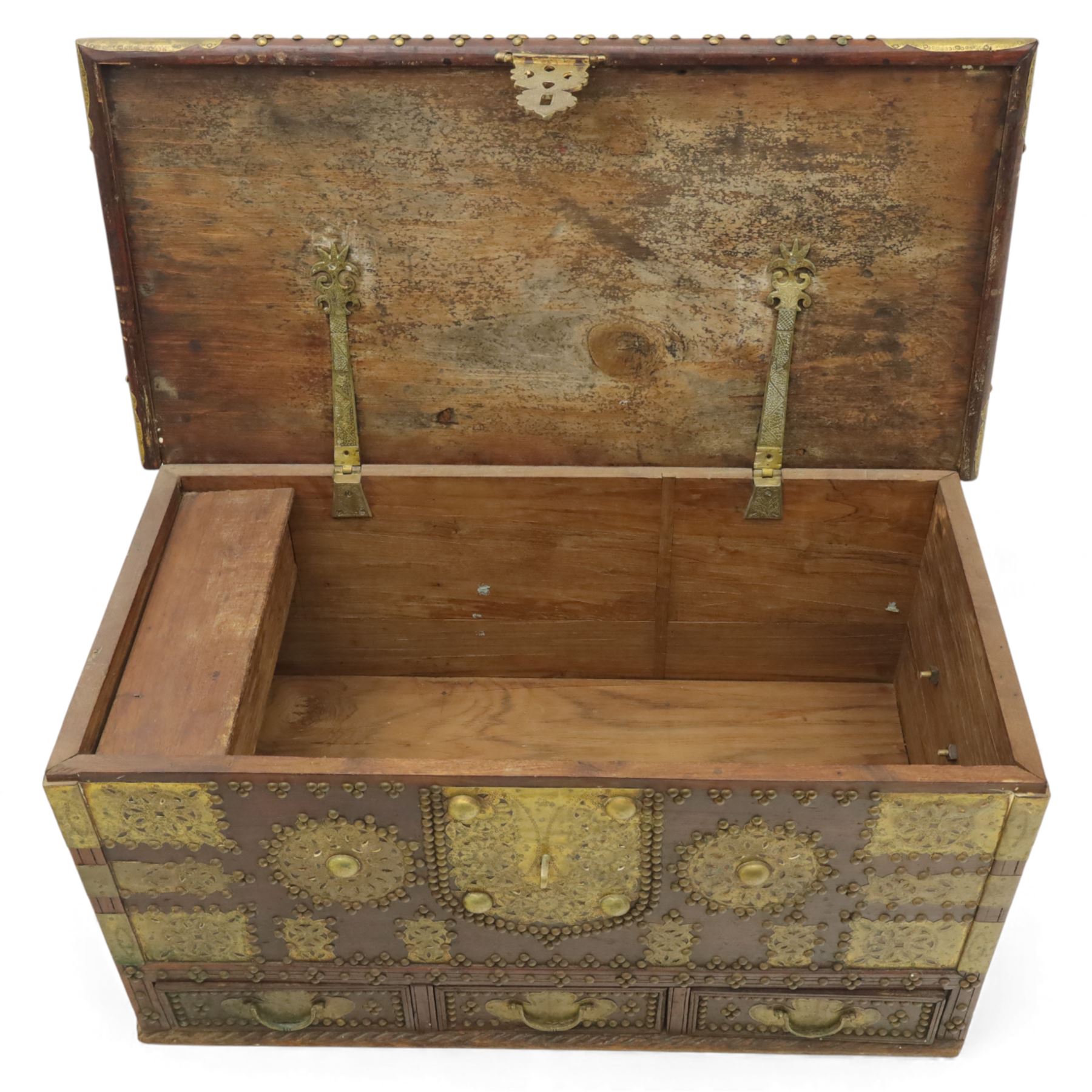 Early 20th century brass-mounted hardwood chest, the hinged top and front richly decorated with applied and studded brass panels and pierced lock escutcheon, revealing a candle box, reinforced with brass corner mounts