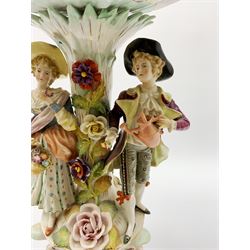 Early 20th century Sitzendorf table centrepiece, modelled as a floral encrusted column flanked by male and female figures, he with watering can, she with basket of flowers, supporting a scrolling, part pierced and floral encrusted basket with hand painted floral sprays to the interior, the whole upon a conforming base, with blue hatched mark beneath, H50cm, basket L36cm